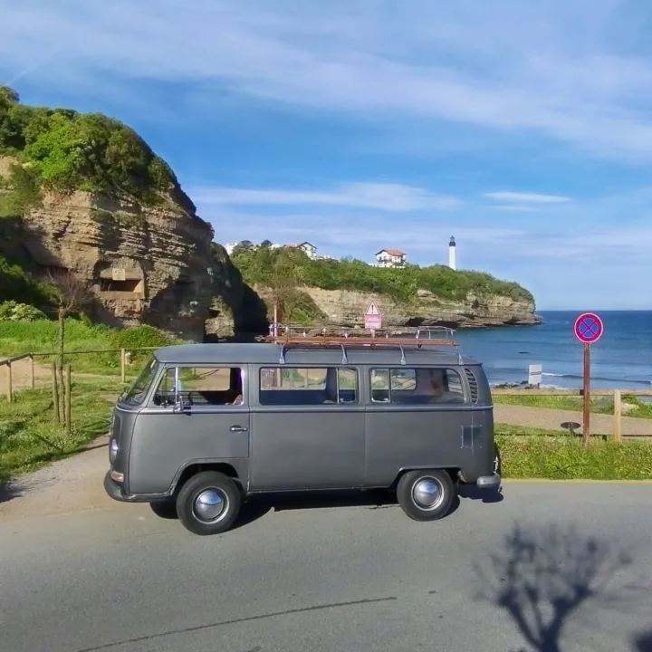 Grey VW camper van parked on a coastal road overlooking the sea & lighthouse. Perfect for your next RV rental trip!. Volkswagen Westfalia Combi 1969