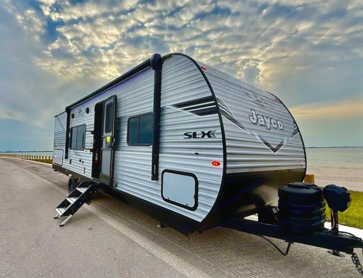 Scenic rv rental: A modern travel trailer awaits by the water, ready for adventure under a dramatic sky.. Jayco 265BHS 2025