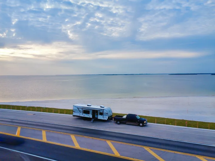 RV rental & truck parked on a coastal road overlooking a calm ocean and sandy beach under a cloudy sky.. Jayco 265BHS 2025