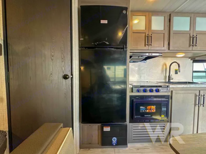 RV rental interior showing a compact kitchen with black fridge, microwave, stove, sink, and wood cabinets.. Keystone Hideout 240bh 2025