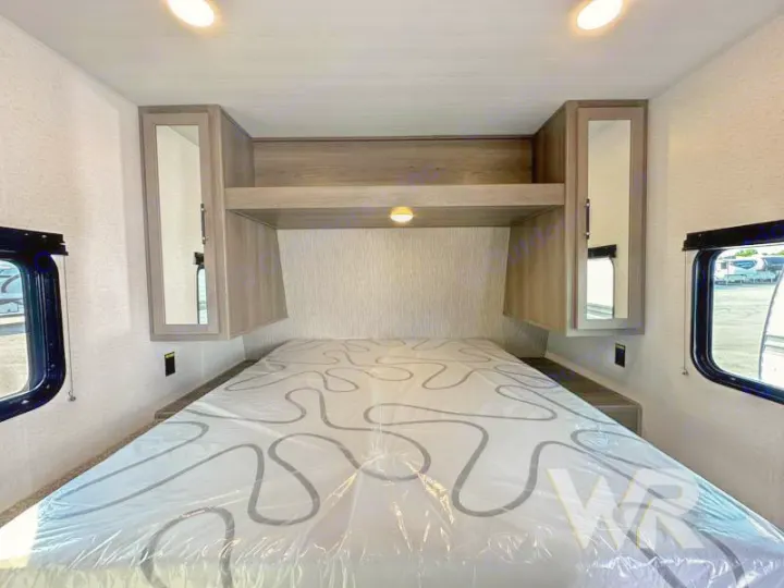 Spacious RV bedroom interior featuring overhead cabinets, side windows, and a comfortable bed. Ideal for your next rv rental.. Keystone Hideout 240bh 2025