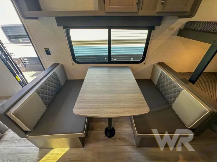 RV rental's cozy dinette with two benches, a table, and a visible bunk bed. Perfect for family adventures!. Keystone Hideout 240bh 2025
