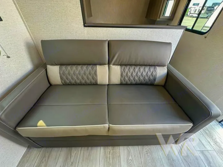 Spacious two-seater RV rental sofa in grey and beige with quilted backrests, offering comfort for your journey.. Keystone Hideout 240bh 2025