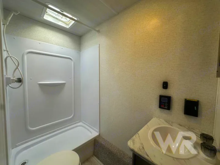 Inside an RV rental: a practical bathroom with a white shower, toilet, and vanity sink, plus controls on the wall.. Keystone Hideout 240bh 2025