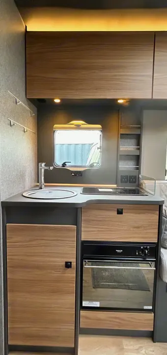 Explore this modern rv rental kitchen featuring a sink, hob, oven/grill, and ample cabinet storage for your next adventure.. GlamperRV DBL 2026