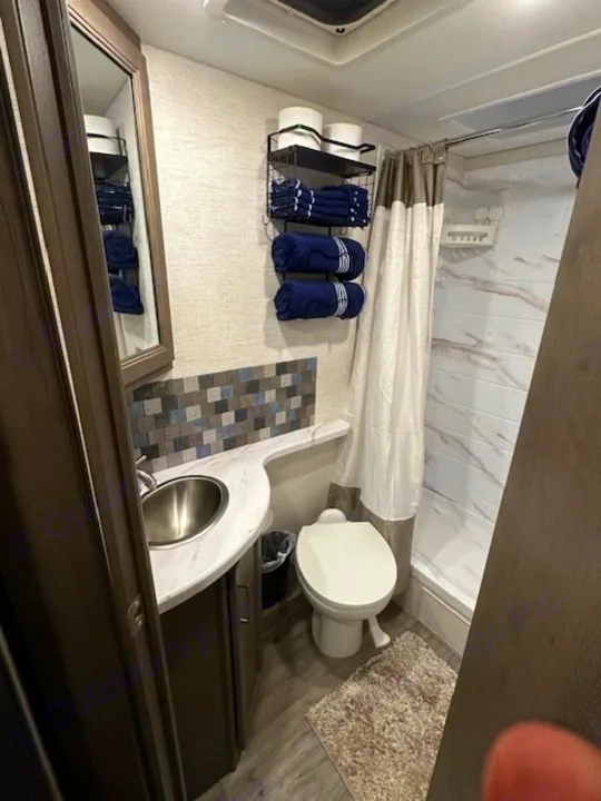 Compact RV rental bathroom interior with sink, toilet, and shower. This well-organized space features towels and a stylish tiled backsplash.. Thor Motor Coach Four Winds 22B 2025