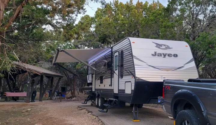 A Jayco travel trailer (RV) for camping or rental, parked at a wooded site with a pickup truck and rustic shelter.. Jayco Jay Flight 2018
