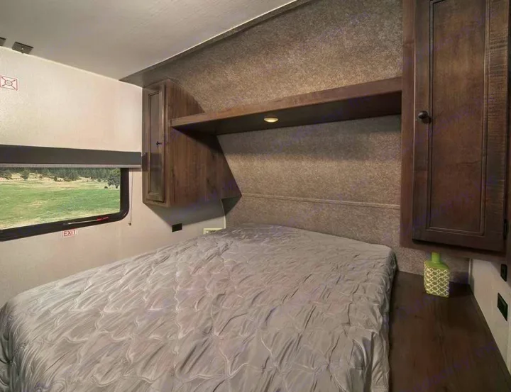 Cozy RV rental bedroom featuring a grey bed, window with nature views, and functional dark wood storage.. Starcraft Autumn Ridge 2022