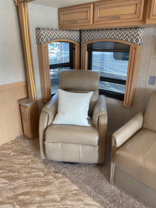 Comfortable RV rental living space featuring a beige leather recliner, patterned window valances, and modern wood cabinetry.. Canyon Star Canyon Star Motorhome 2020