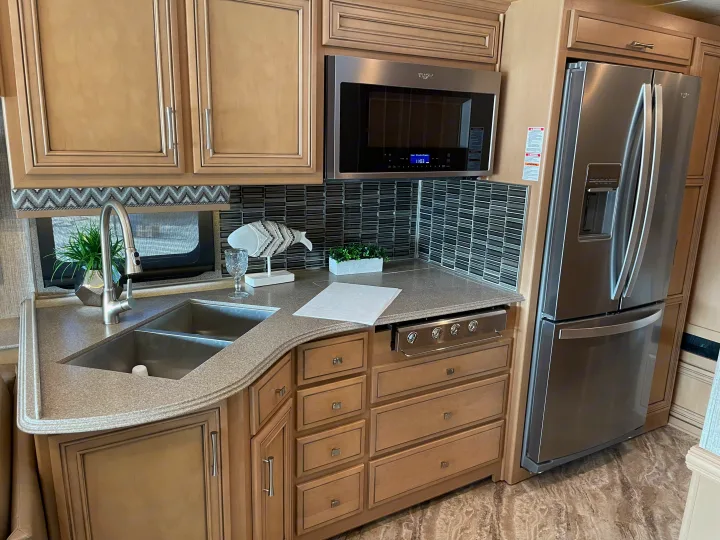 Sleek RV rental kitchen with a large fridge, microwave, double sink, light cabinets, and tiled backsplash.. Canyon Star Canyon Star Motorhome 2020