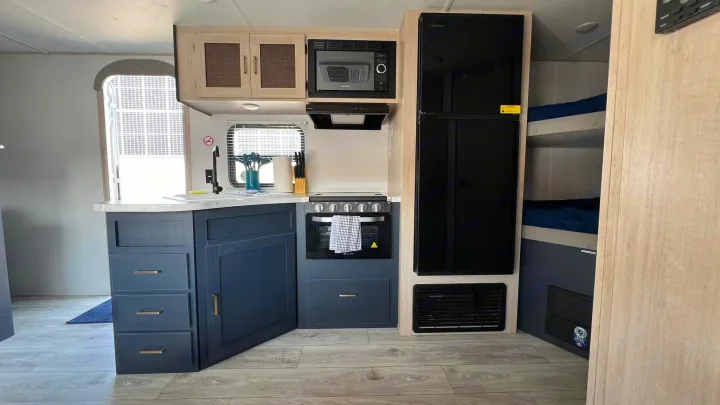 Spacious RV rental interior showcasing a modern kitchen with blue cabinets, appliances, and cozy bunk beds.. Prime Time Avenger 2024