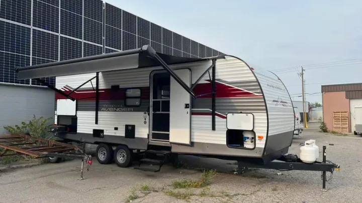 This white & red travel trailer with awning extended is perfect for your next RV rental adventure. Parked near solar panels.. Prime Time Avenger 2024