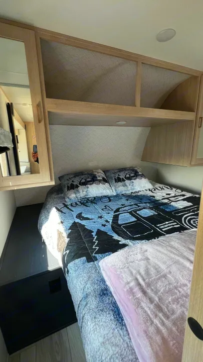 Cozy RV rental bedroom featuring a camping-themed bed, overhead storage, and mirror. Ideal for a comfortable stay.. Prime Time Avenger 2024