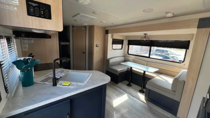 Inside a bright RV rental: modern kitchen with sink, plus a comfy dinette with windows, perfect for travel.. Prime Time Avenger 2024