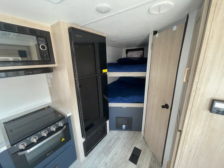 Compact RV rental interior featuring a full kitchen with microwave, stove, fridge, and cozy bunk beds.. Prime Time Avenger 2024