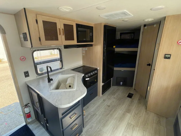 Modern RV rental interior featuring a full kitchen with sink, stove, microwave, and bunk beds. Perfect for camper adventures!. Prime Time Avenger 2024