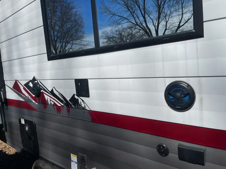 RV rental exterior: white siding, mountain graphics, window reflections, outdoor speaker, & TV mount. Ready for your adventure.. Forest River Campsite reserve 27MR 2025