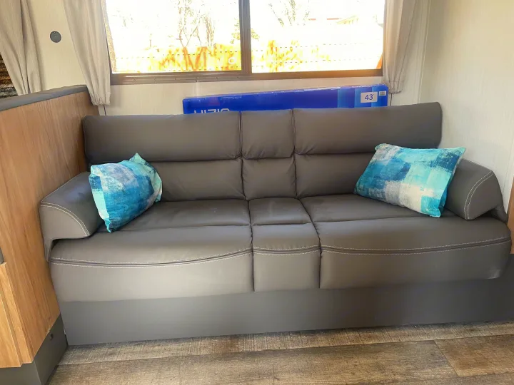 RV rental interior: A dark gray sofa with two light blue pillows offers comfortable seating. Wooden cabinetry is visible to the left.. Forest River Campsite reserve 27MR 2025