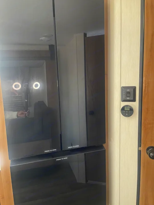 RV rental: Modern black appliance with 'PRESS TO OPEN' text, next to RV slide room and Furrion 64° thermostat controls.. Forest River Campsite reserve 27MR 2025