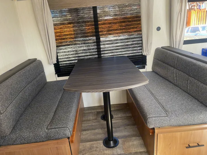 Spacious RV rental dinette with cozy gray bench seating and a dark wood table, perfect for meals on the go.. Forest River Campsite reserve 27MR 2025