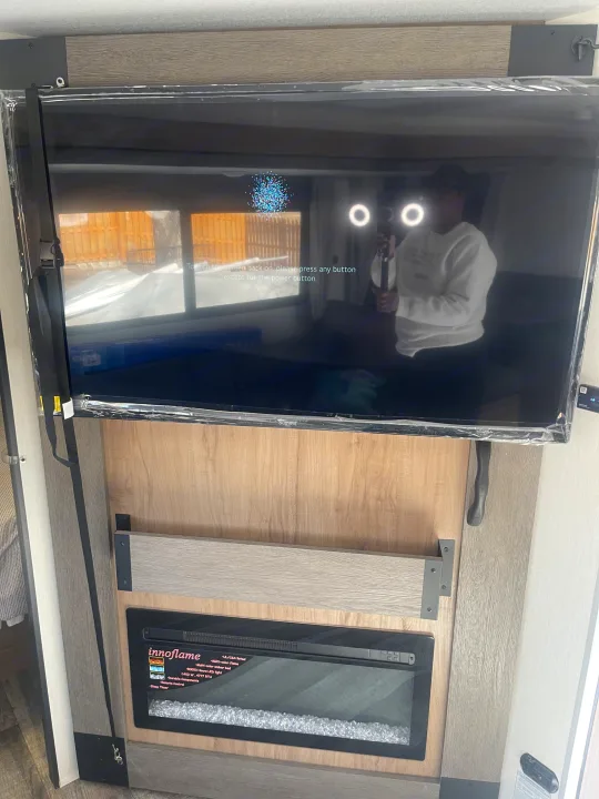 RV rental: TV showing screen instructions & person's reflection, with protective film. Electric fireplace below.. Forest River Campsite reserve 27MR 2025