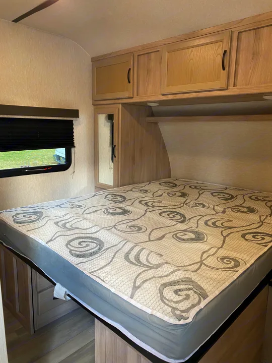 This RV rental bedroom features light wood cabinets, a patterned mattress, and a window with a pulled-down blind.. Coachmen Spirit Ultra light 2021