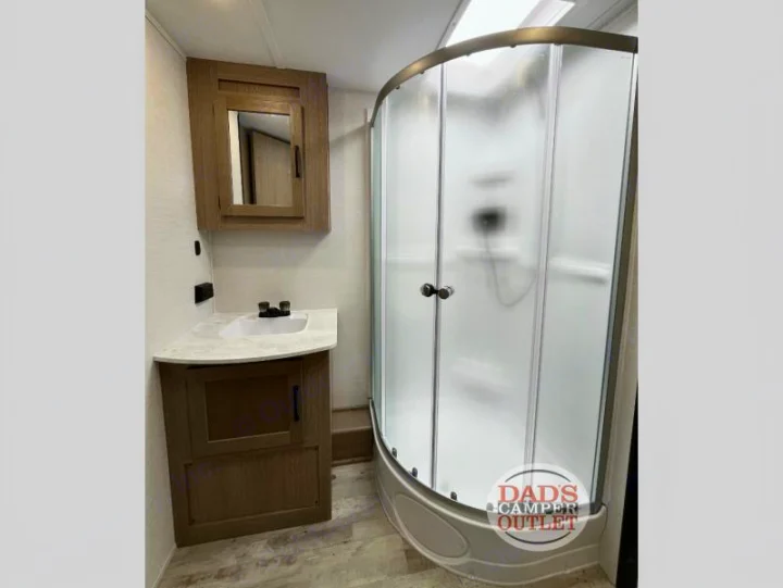 Inside an RV rental bathroom: a compact vanity with sink & mirrored cabinet, alongside a modern rounded frosted glass shower.. Gulf Stream Innsbruck 2024