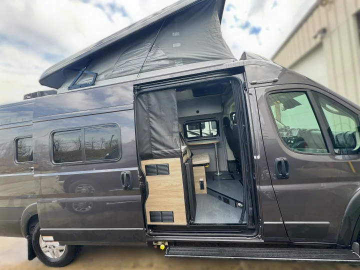 Pop-top rv rental with open side door revealing its compact living area, complete with a table and seating.. Winnebago Solis 2021