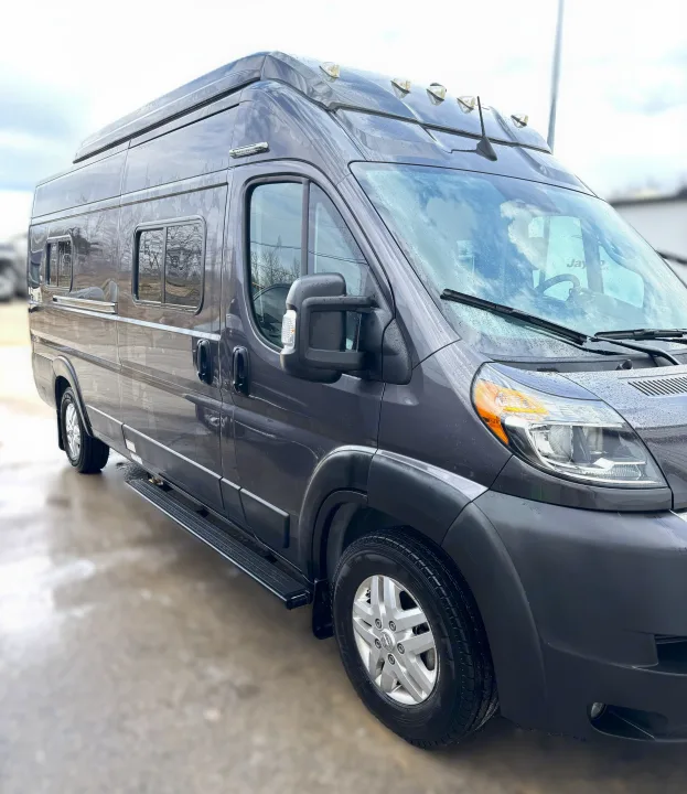 This dark gray RV rental camper van, glistening with raindrops, is parked outdoors, ready for your next road trip adventure.. Winnebago Solis 2021