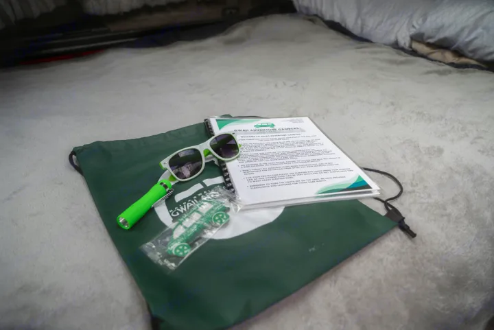 Your RV rental adventure starts! Welcome kit with sunglasses, flashlight, toy, & camper info on a green bag, ready for exploration.. Mitsubishi Delica 2000