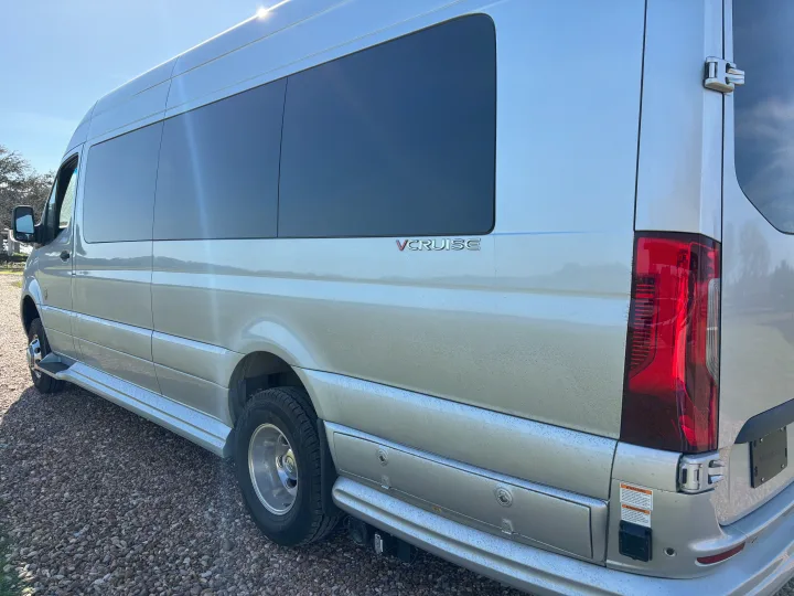 Side/rear view of a silver VCRUISE camper van, perfect for your next rv rental. Parked on gravel under sunlight.. Mercedes-Benz OG Luxury Coach V Cruis 2025