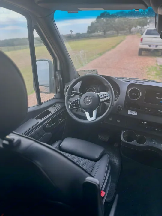 View from inside a spacious Mercedes-Benz RV rental van, featuring its dashboard, steering wheel, and quilted leather seats.. Mercedes-Benz OG Luxury Coach V Cruis 2025
