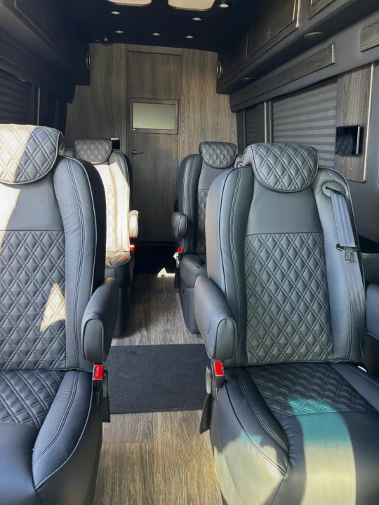 Spacious luxury RV rental interior features plush black leather captain's chairs, wood paneling, and bright cabin lighting.. Mercedes-Benz OG Luxury Coach V Cruis 2025
