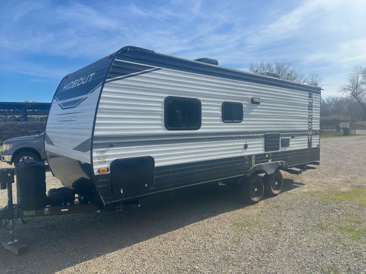 This black and white Keystone Hideout travel trailer RV rental sits on gravel under a blue sky, perfect for your next trip.. Keystone Hideout 2022