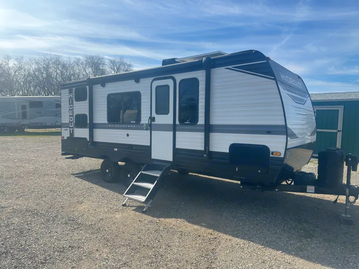 Modern white & black Keystone Hideout travel trailer, an ideal RV rental. Parked on gravel with steps down & solar panel on roof.. Keystone Hideout 2022