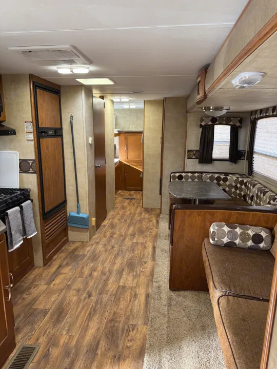 RV rental interior: kitchen with stove & fridge, dining dinette with patterned cushions, & wood-look floor in the hallway.. Keystone RV Passport Grand Touring 2014