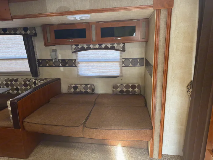 Inside this rv rental, you see a cozy living space with convertible sofas, overhead storage, and patterned decor.. Keystone RV Passport Grand Touring 2014