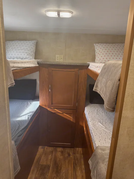 Comfortable bunk beds with central storage in a well-lit RV rental interior. Ideal for families on their travel adventures.. Keystone RV Passport Grand Touring 2014