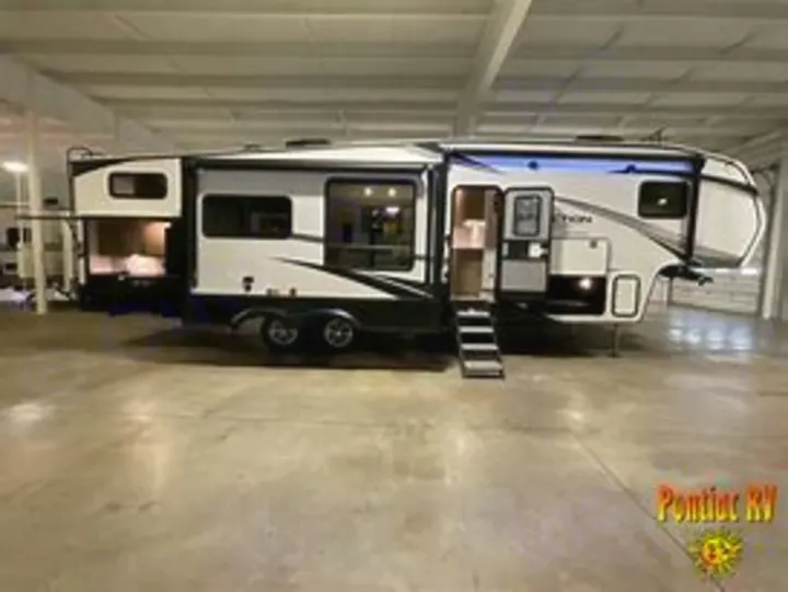 A large, modern white and black fifth-wheel RV rental with slide-outs extended and door open, parked indoors on concrete.. Grand Design Reflection 2023
