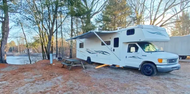White RV rental at a scenic lakeside campsite with an extended awning and picnic table.. Winnebago Outlook 2007