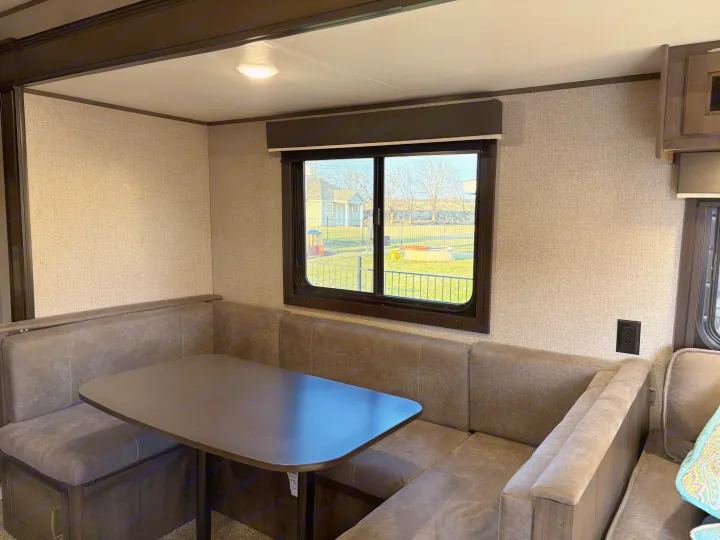 RV rental dinette: comfortable U-shaped seating and dark table with a window view to a yard. Ideal for meals.. Jayco Jay Flight SLX 2021