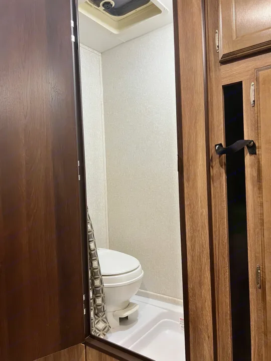 Compact RV rental bathroom showcasing a white toilet, shower pan, ceiling vent, and dark wood accents.. Jayco Hummingbird 2019