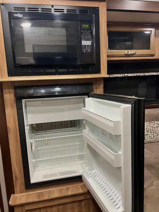 Compact kitchen in an RV rental, showing a High Pointe microwave and an open Dometic refrigerator with shelves.. Jayco Hummingbird 2019