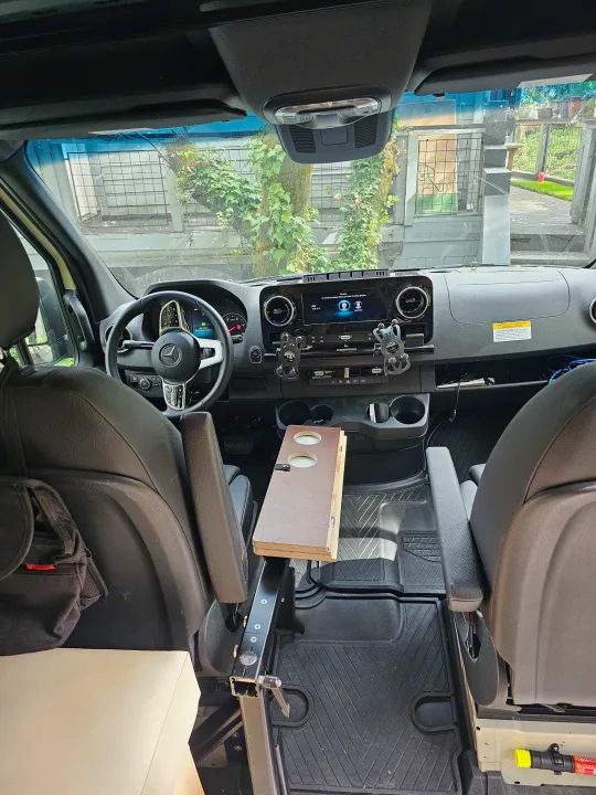 RV rental camper van interior: modern dashboard, swiveled front seats, and a custom table. View from the back cabin.. mercedes 144 High Roof AWD 2024