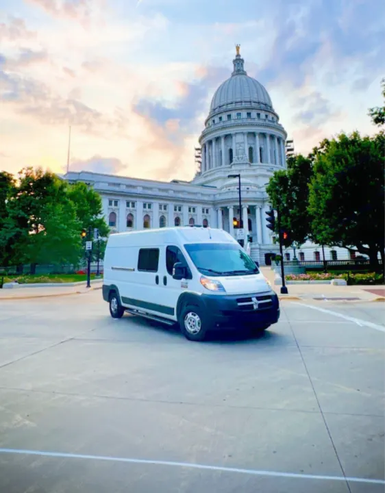 A white RV rental van on a street, with the majestic Wisconsin State Capitol's dome rising behind it.. Dodge Ram 1500 2014