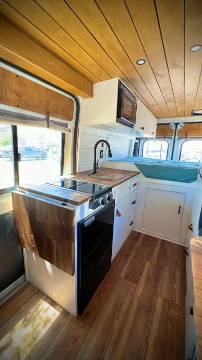 Spacious & modern RV rental interior with wood ceiling, full kitchen, and bed. Perfect for van life adventures!. Dodge Ram 1500 2014