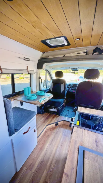 Inside a cozy RV rental: dining table set with blue dishes, kitchenette, and driver's area, featuring wood floors and ceiling.. Dodge Ram 1500 2014