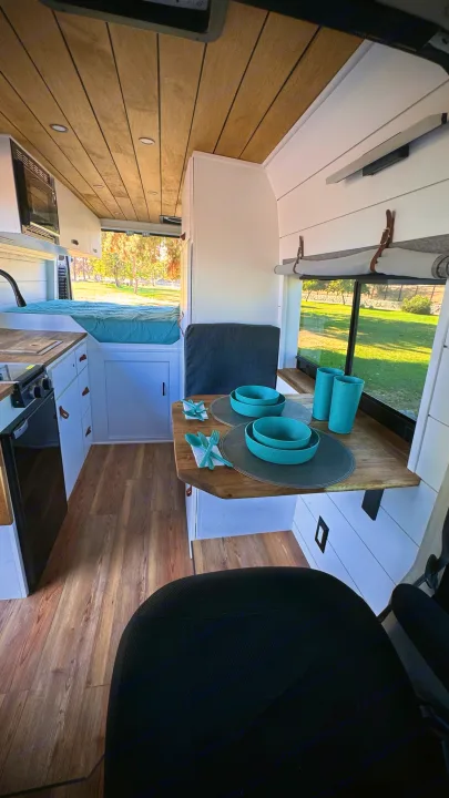 Inside a stylish **rv rental**, offering a bright kitchen, dining area with teal dishes, and a comfortable bed.. Dodge Ram 1500 2014