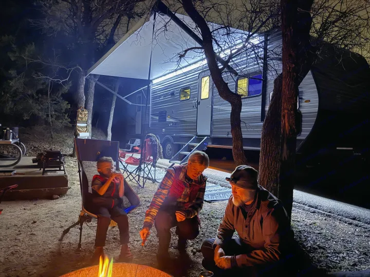 Nighttime family camping trip: a warm campfire illuminates a family beside their brightly lit RV rental.. Jayco Jay Flight SLX 2021