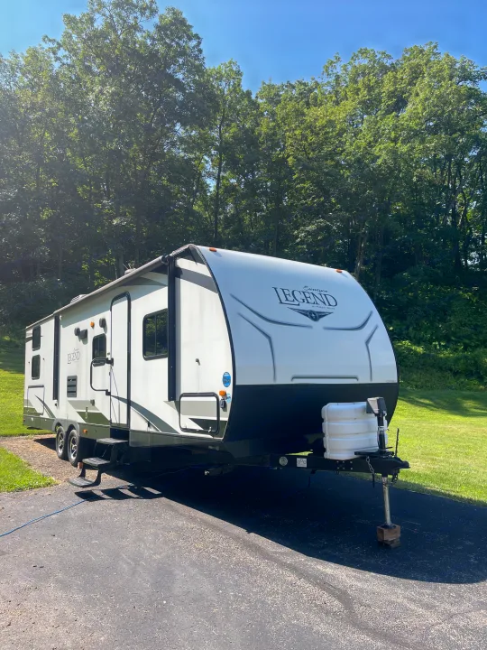 White Legend RV rental parked on a sunny driveway with green trees and blue sky in the background.. Forest River Surveyor Legend 2019